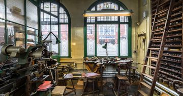 Workshop with machinery, a workbench in front of a window and wooden shelves with a ladder
