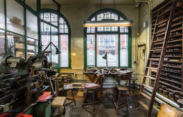Workshop with machinery, a workbench in front of a window and wooden shelves with a ladder