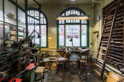 Workshop with machinery, a workbench in front of a window and wooden shelves with a ladder
