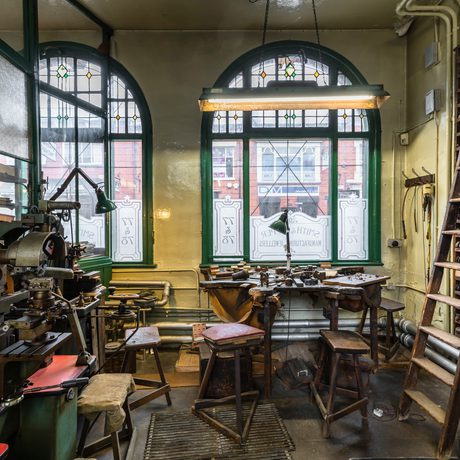 Workshop with machinery, a workbench in front of a window and wooden shelves with a ladder