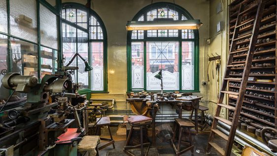 Workshop with machinery, a workbench in front of a window and wooden shelves with a ladder