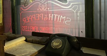 Telephone and paper on table in front of a window with Smith & Pepper sign on it.