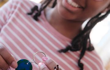 A smiling child holding her finished jewellery design.