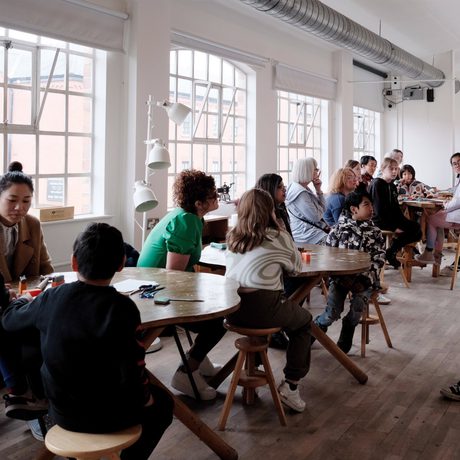 A group of adults and children sitting at tables listening to members of staff talking.