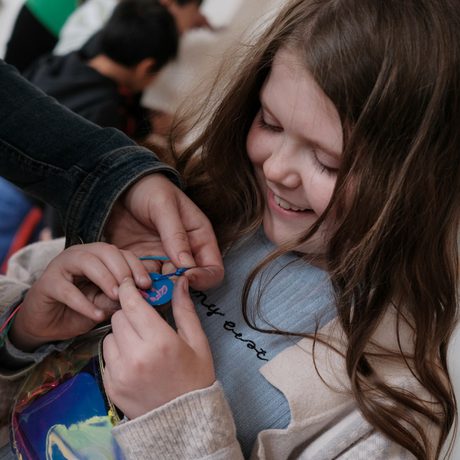 A happy child wearing and holding their finished pendant necklace.