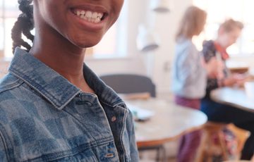 A smiling child holding her finished piece of jewellery.