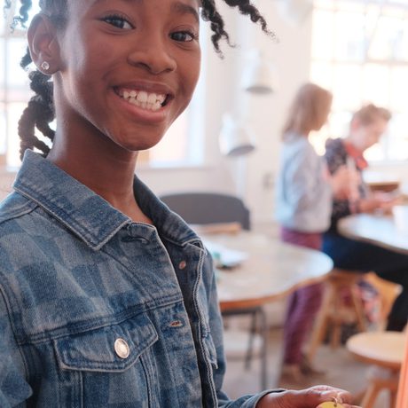 A smiling child holding her finished piece of jewellery.