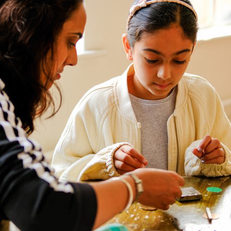 An adult and a child in a hands-on jewellery making activity at a table.