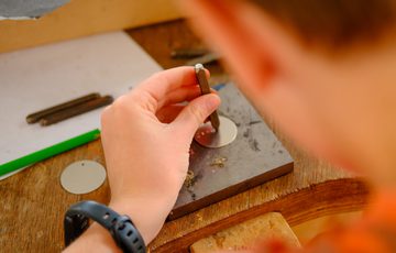 Person working with metal discs and tools on a wooden workbench.