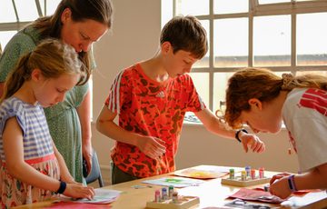Children focused on craft activity with adult supervision near a window.