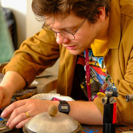 A focused staff member working on colourful jewellery pieces on a wooden table.