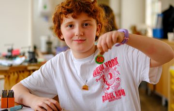 Young child with curly hair showcasing a small disc jewellery project indoors, smiling gently.