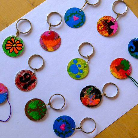 Colourful, handmade keychains with various painted designs arranged on white paper.