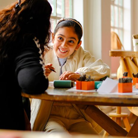 A child and adult engage in a creative activity together at a wooden table.