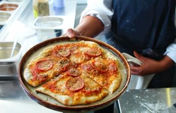 A chef holds a plate containing a pepperoni pizza