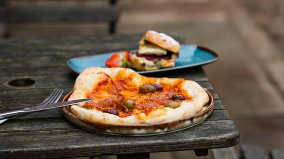 Pizza with olives on a plate resting on a wooden outdoor table