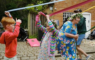 Two children holding the ribbons of a may pole.