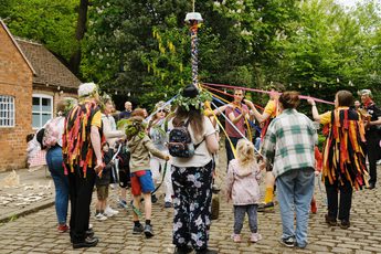 A group of morris dancers and visitors dancing around the may pole.