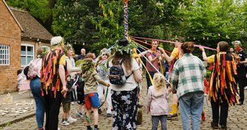 A group of morris dancers and visitors dancing around the may pole.