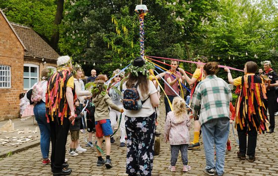 A group of morris dancers and visitors dancing around the may pole.