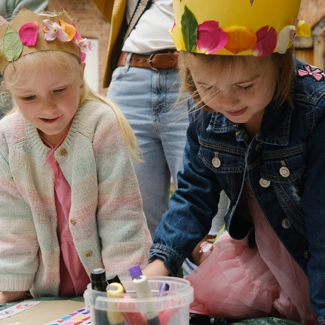 Two children drawing while wearing paper crowns.