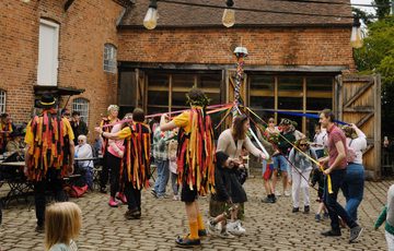 A group of Morris dancers and members of the public dancing around the may pole.