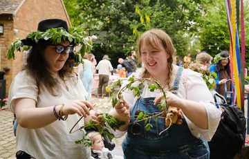 Two adults smiling and making flower headbands.