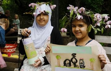 Two smiling children wearing handmade flower headbands holding their painted artworks.