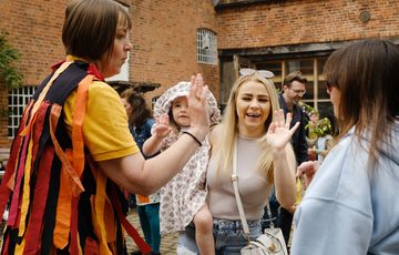 A smiling adult holding a child dancing and giving a high five to a morris dancer.