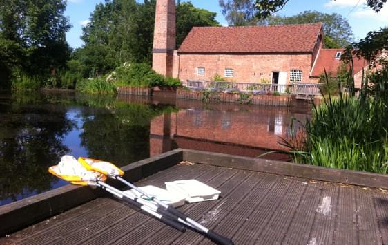 Pond dipping kit including nets and plastic trays in front of Sarehole Mill millpond.