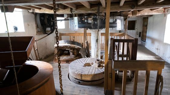 Timber-beamed interior workings of a mill, showing the millstones