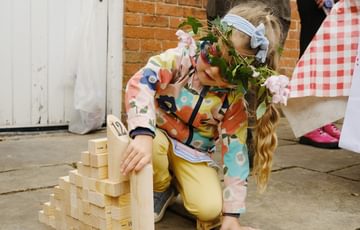 A child wearing a flower headband while playing a small wooden garden game.