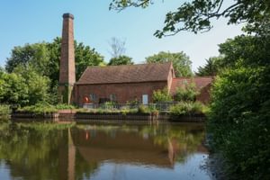 View of Mill in front of pond surrounded by trees.