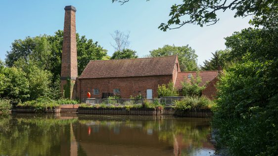 View of Mill in front of pond surrounded by trees.