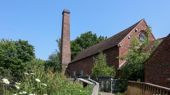 Path to brick-built water mill building surrounded by plants and trees.