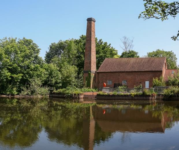 Wide view of Mill in front of a large pond surrounded by trees.
