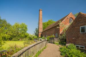 Path to brick-built water mill buildings in front of a green pond