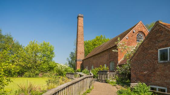 Path to brick-built water mill buildings in front of a green pond