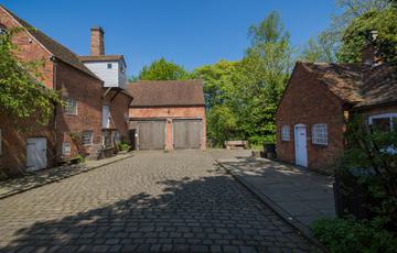 A two storey brick building with single storey outbuilding opposite across a cobbled courtyard.