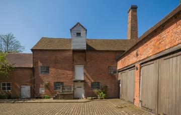Two brick-built buildings meet to from a corner of a brick-paved courtyard.
