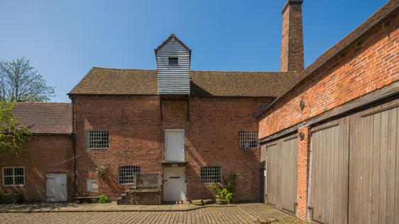 Two brick-built buildings meet to from a corner of a brick-paved courtyard.