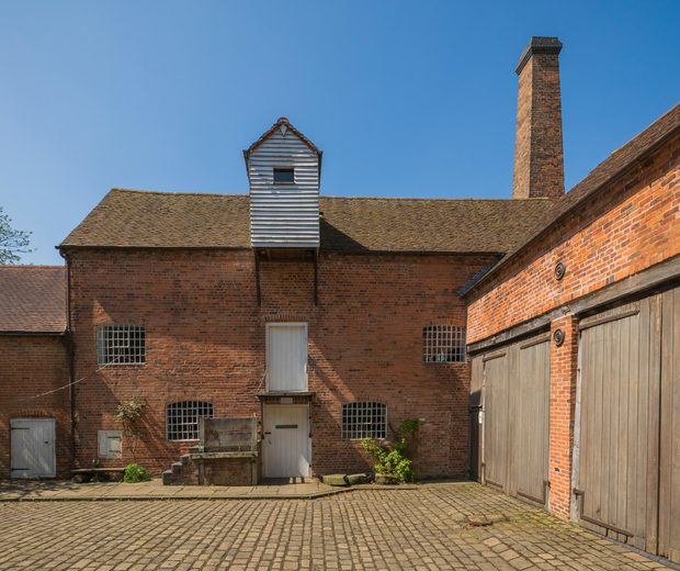 Two brick-built buildings meet to from a corner of a brick-paved courtyard.