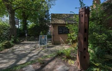 A sculpture of a tower outside surrounded by shrubs and trees.