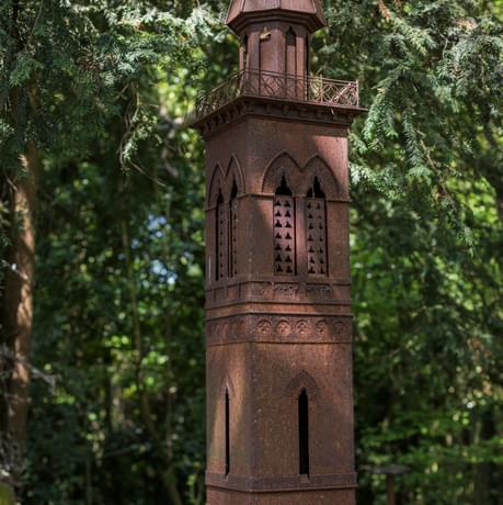 A sculpture of a tower, shrubs are in the background.