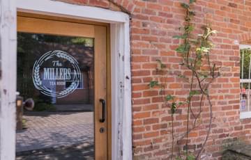 Part of a brick building with a glazed door with sign on it that reads The Millers Tearoom.