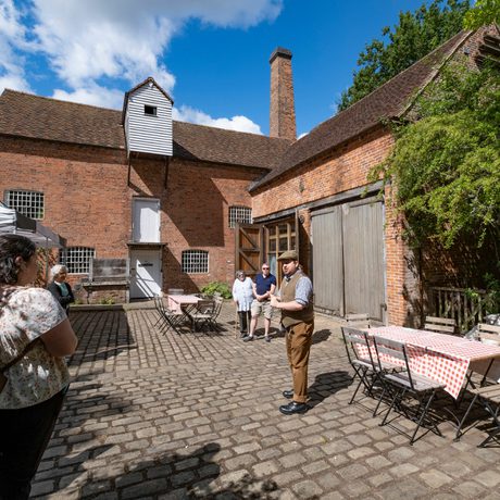 A man outside a brick building presenting to a small group of people.
