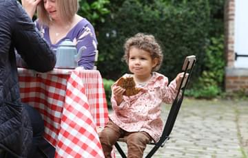 A child is sitting at a table with two adults. the child is holding a large cookie.