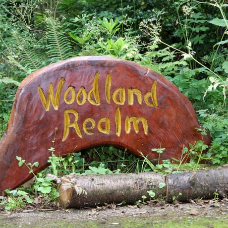 A wooden sculpture with the words 'Woodland Realm' carved into it.