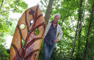 A man standing next to a wooden sculpture of a large leaf.