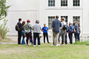 A group of people on a tour, standing on the grass with a white georgian house in the background